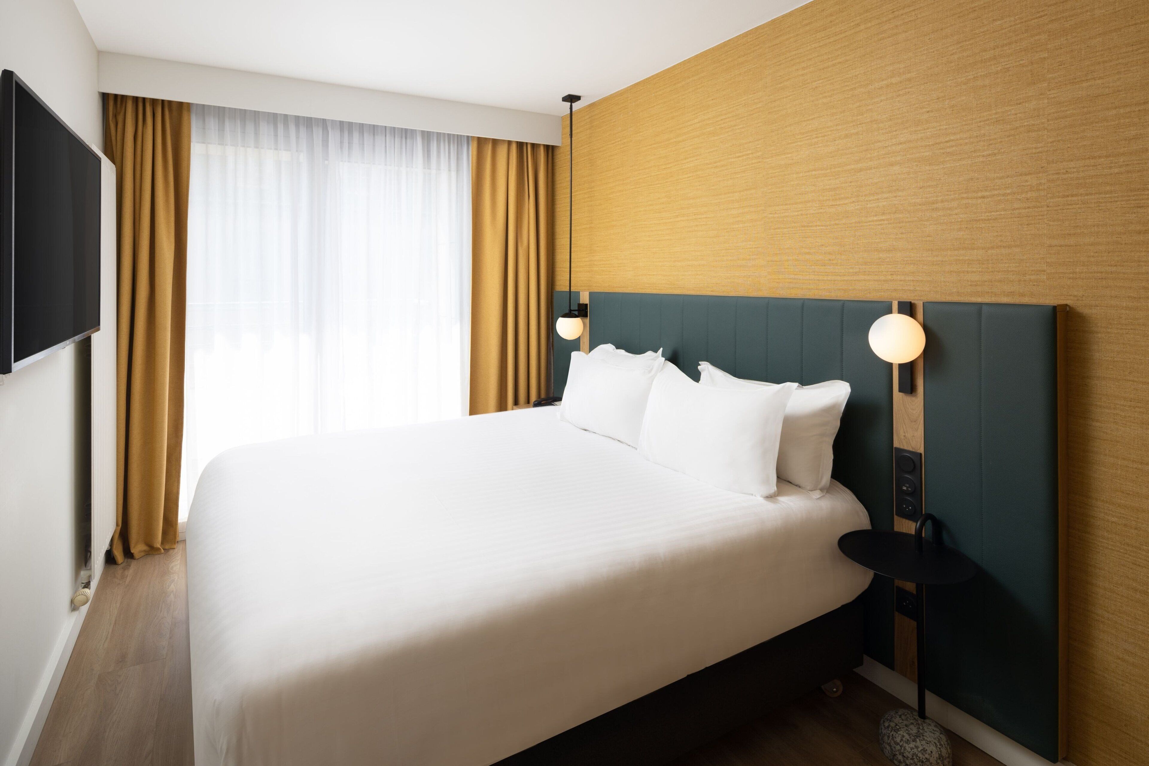 A neatly made bed with white linens, a wooden headboard, and a small bedside table with a lamp.