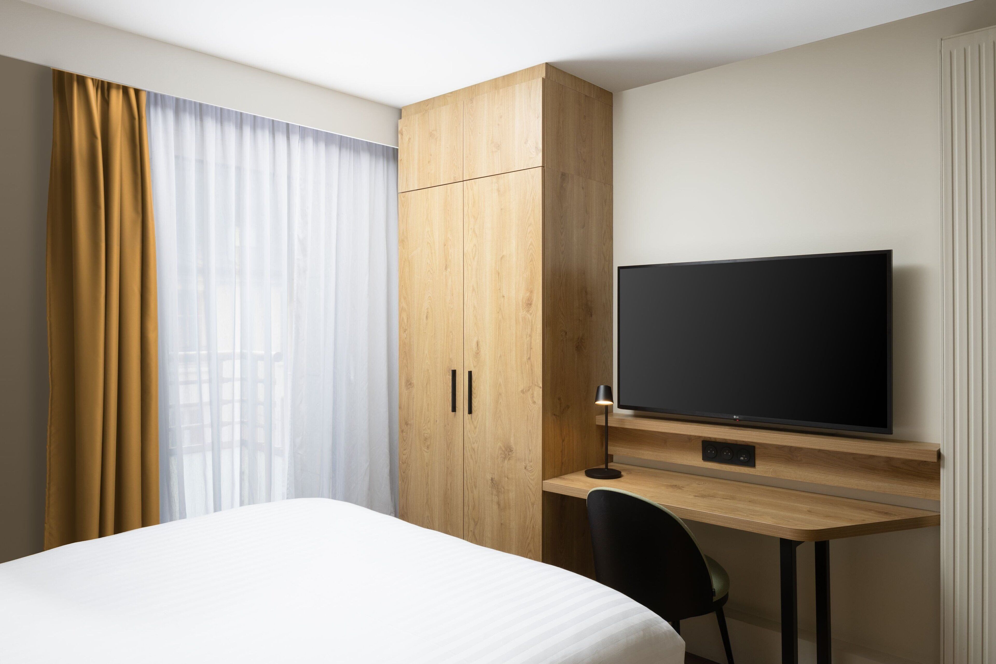 A hotel room with a bed, a desk with a television, and a wardrobe.