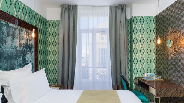 Une chambre d’hôtel avec un lit, un bureau et une fenêtre avec des rideaux.
