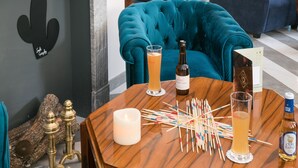 Un salon chaleureux avec un canapé de couleur turquoise, une table basse en bois sur laquelle sont posées des boissons et une bougie, et une cheminée décorée d’un cactus.