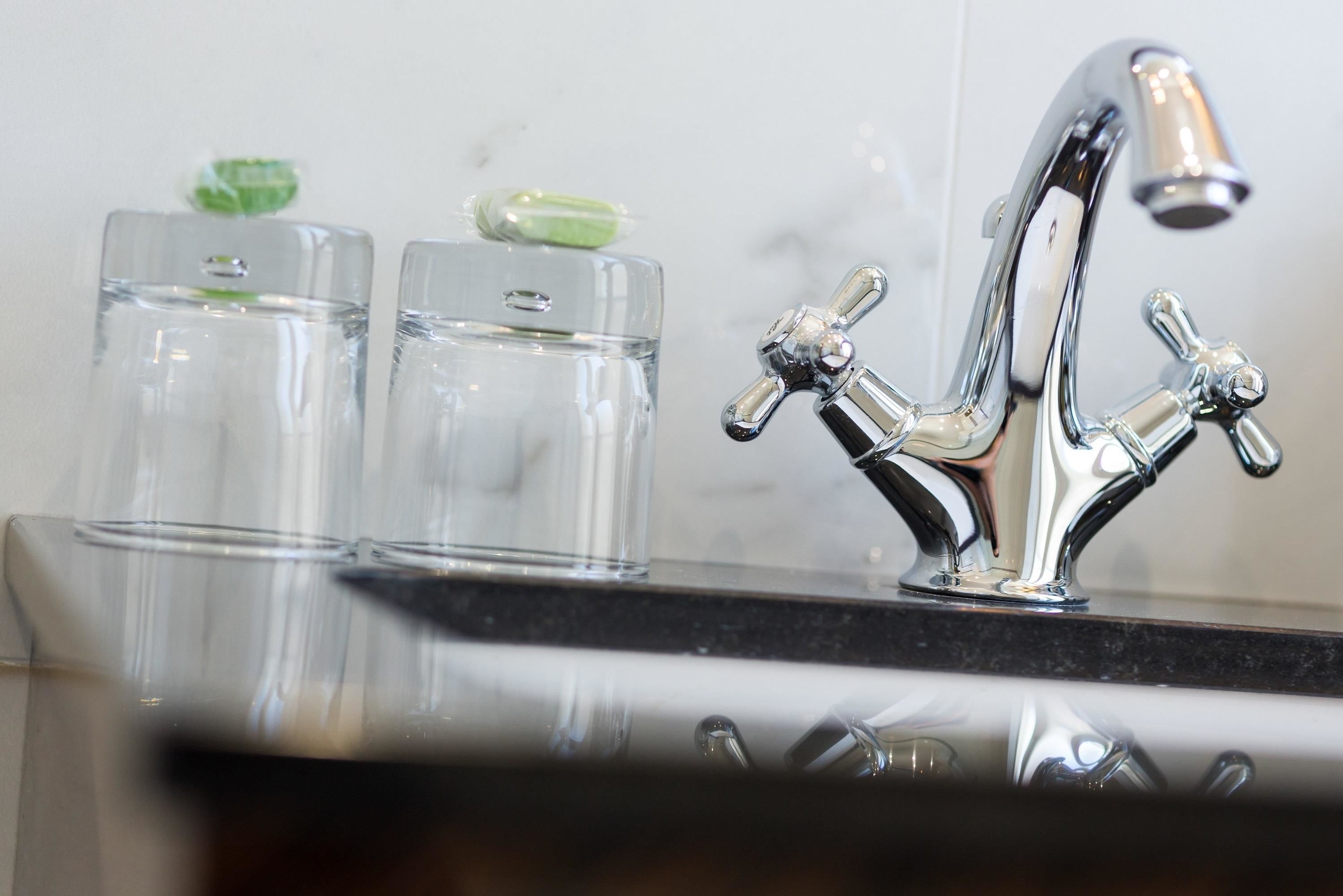 Une salle de bain moderne avec un robinet chromé et deux récipients en verre transparent contenant des objets verts.