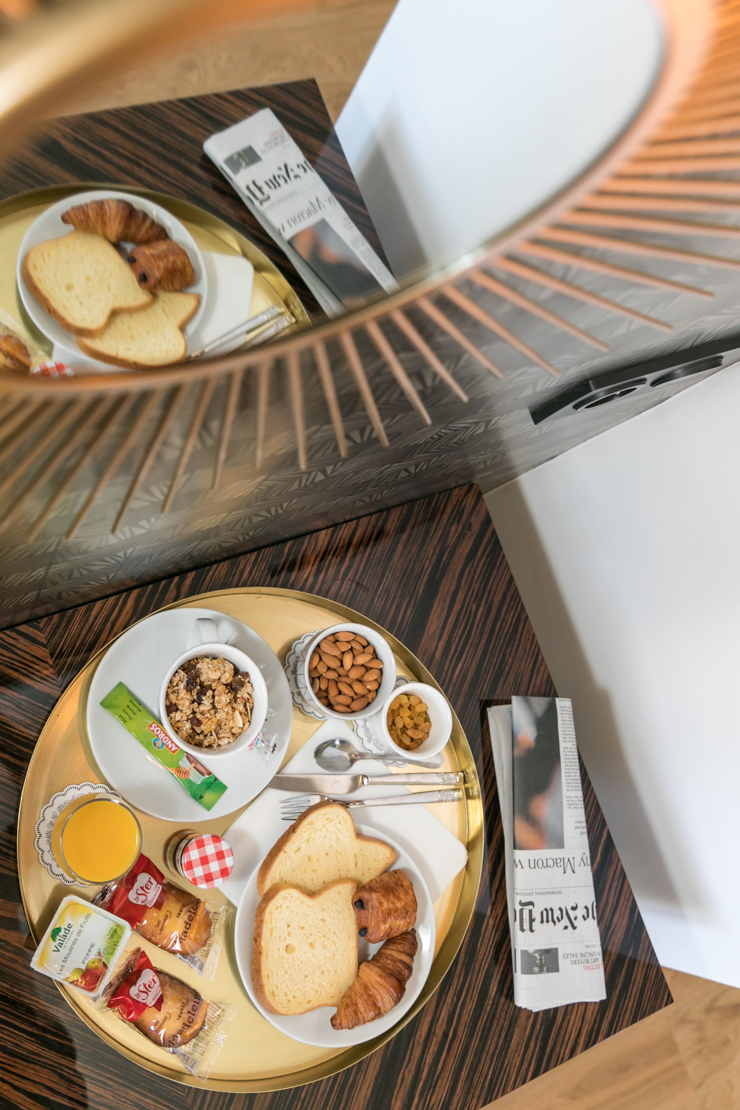 Een ontbijtplateau met croissants, amandelen en een krant op een houten tafel.