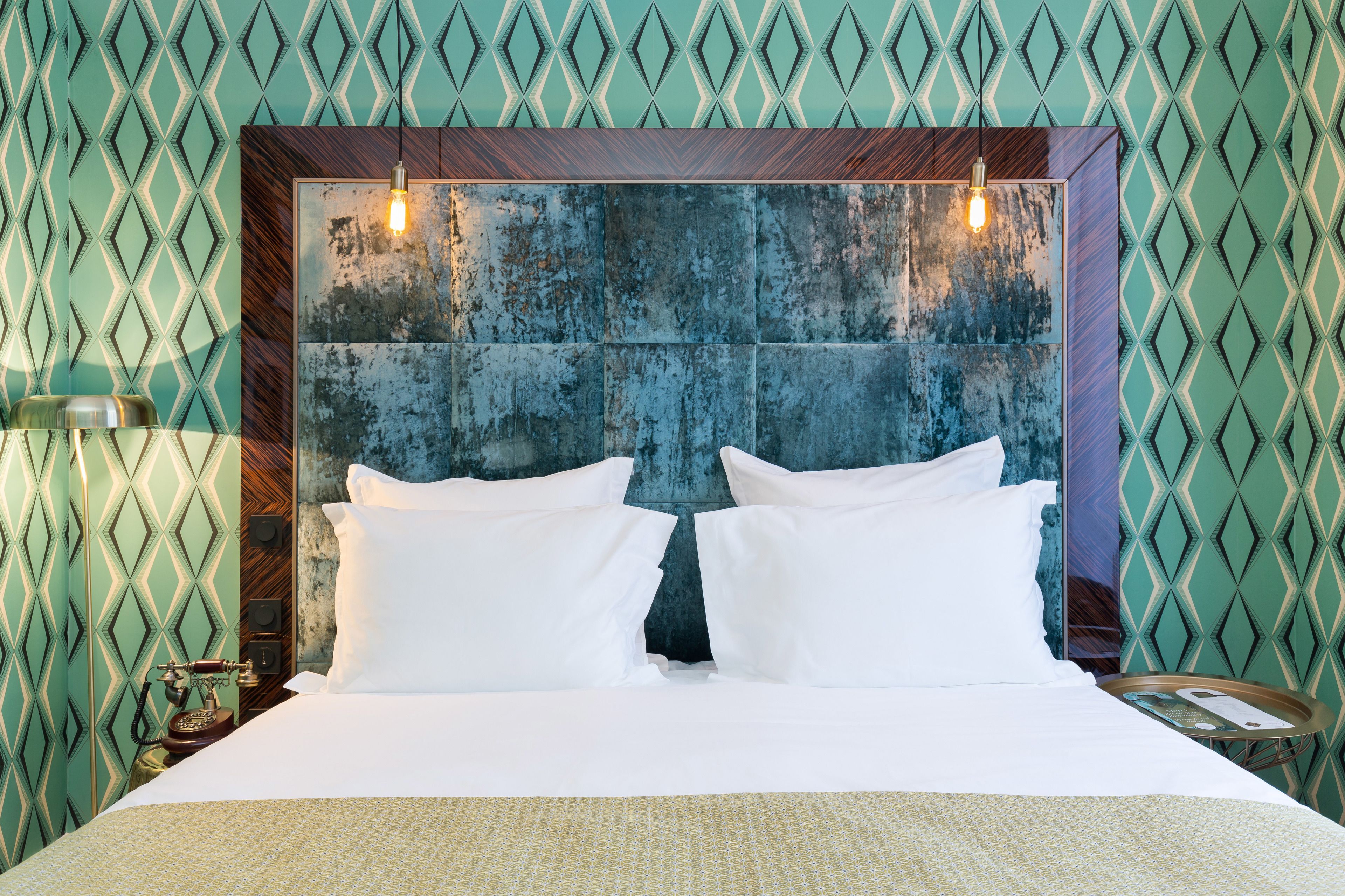Habitación de hotel con una cama grande, cabecera de madera y un papel tapiz estampado.