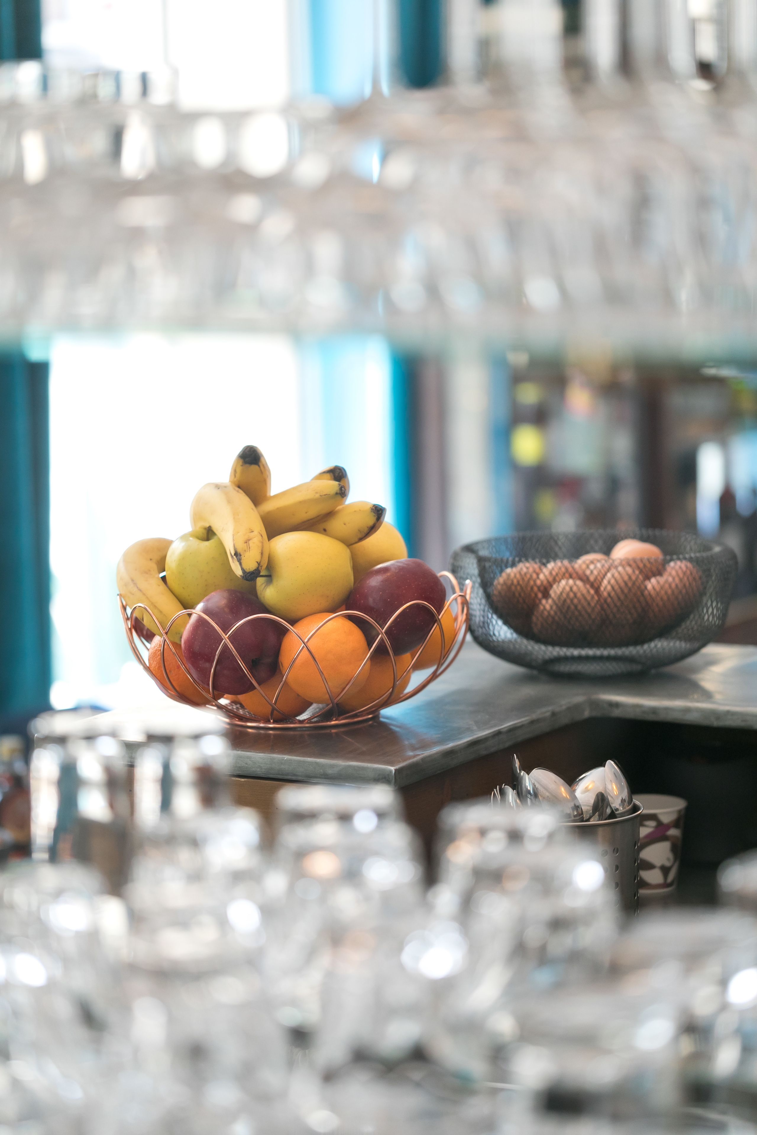 Un frutero con plátanos, manzanas y naranjas sobre una barra.