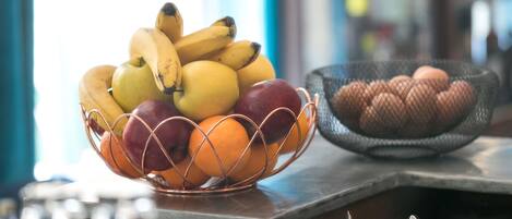 Un frutero con plátanos, manzanas y naranjas sobre una barra.