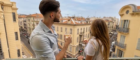 A couple on a balcony overlooking a cityscape with buildings and a street.