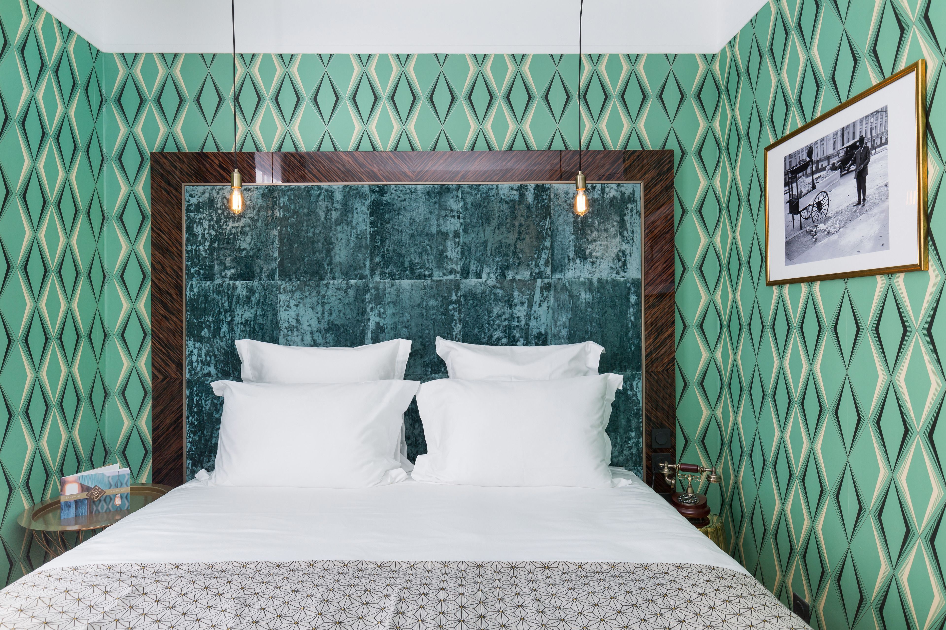 Habitación de hotel con pared de estampado geométrico, una cama grande con ropa blanca y un cuadro en la pared.
