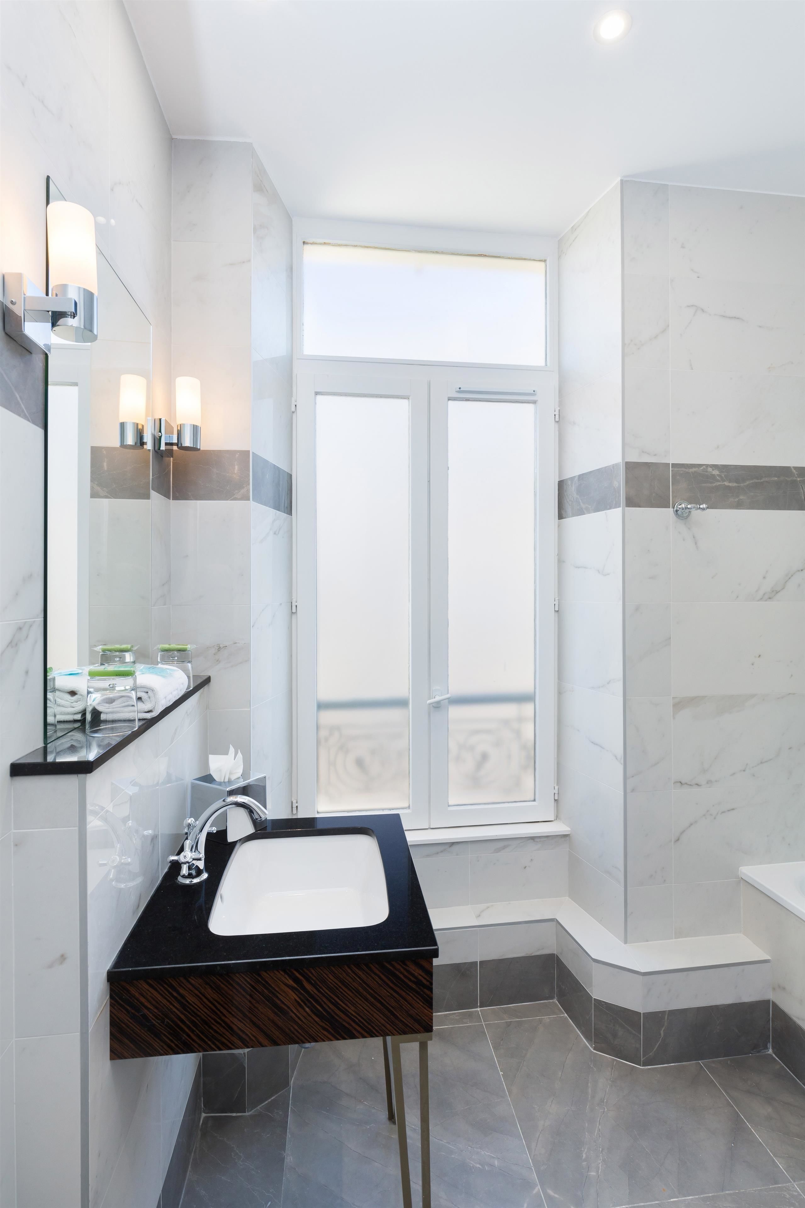 Un baño moderno con lavamanos de superficie negra, un espejo con luces empotradas en la pared y una ventana que proporciona luz natural.
