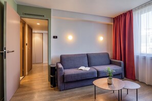 A modern room with a grey sofa, a small round table, and a potted plant. - Citadines Place d’Italie Paris (Paris)