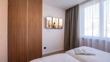 Habitación de hotel con cama, armario, televisor montado en la pared y ventana con cortinas.