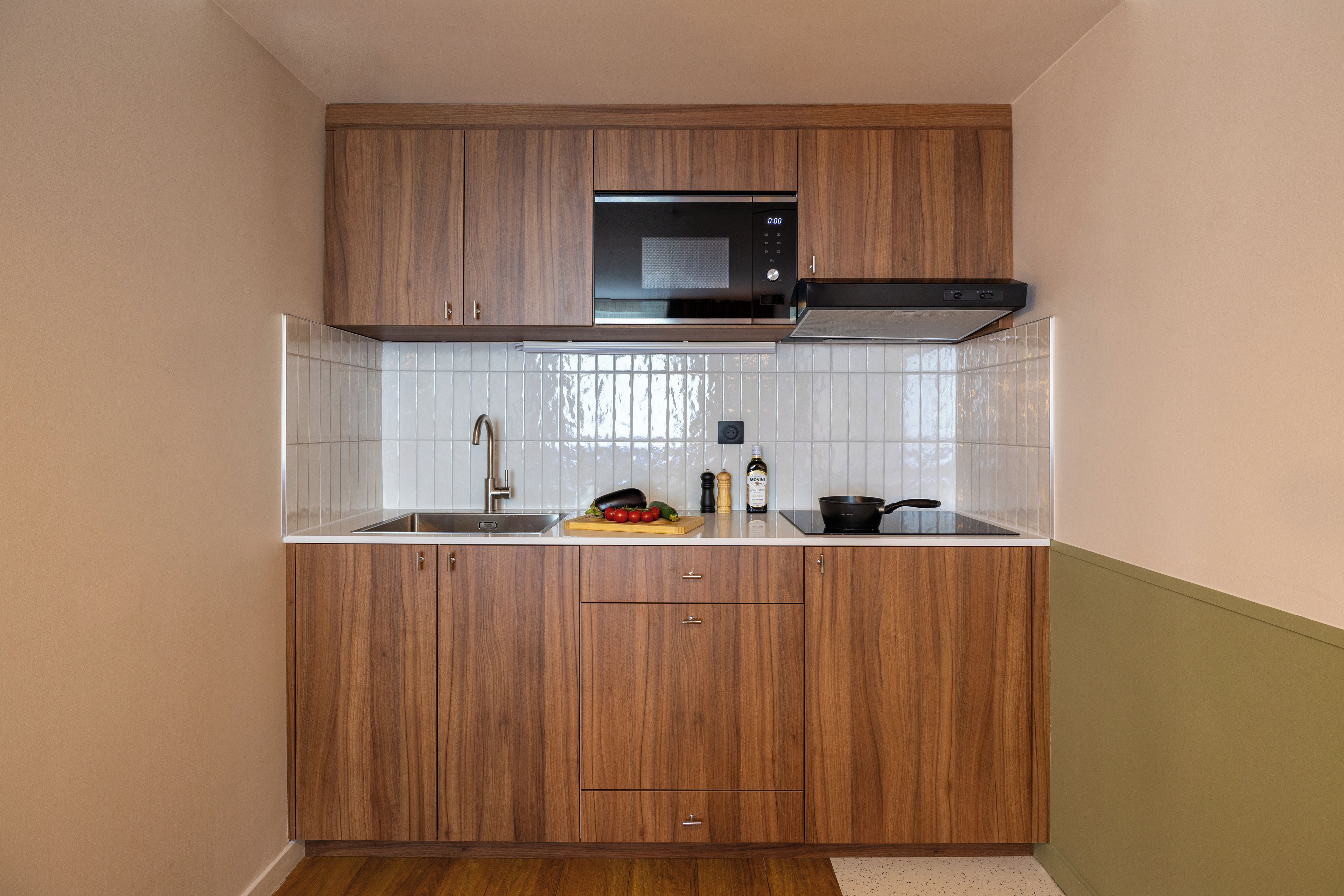 Una cucina compatta con mobili in legno, un forno a microonde, un lavello e un tagliere con verdure.