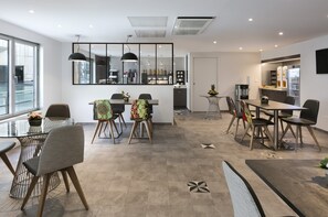 A modern dining area with a large table, chairs, and a kitchen in the background. - Citadines Place d’Italie Paris (Paris)