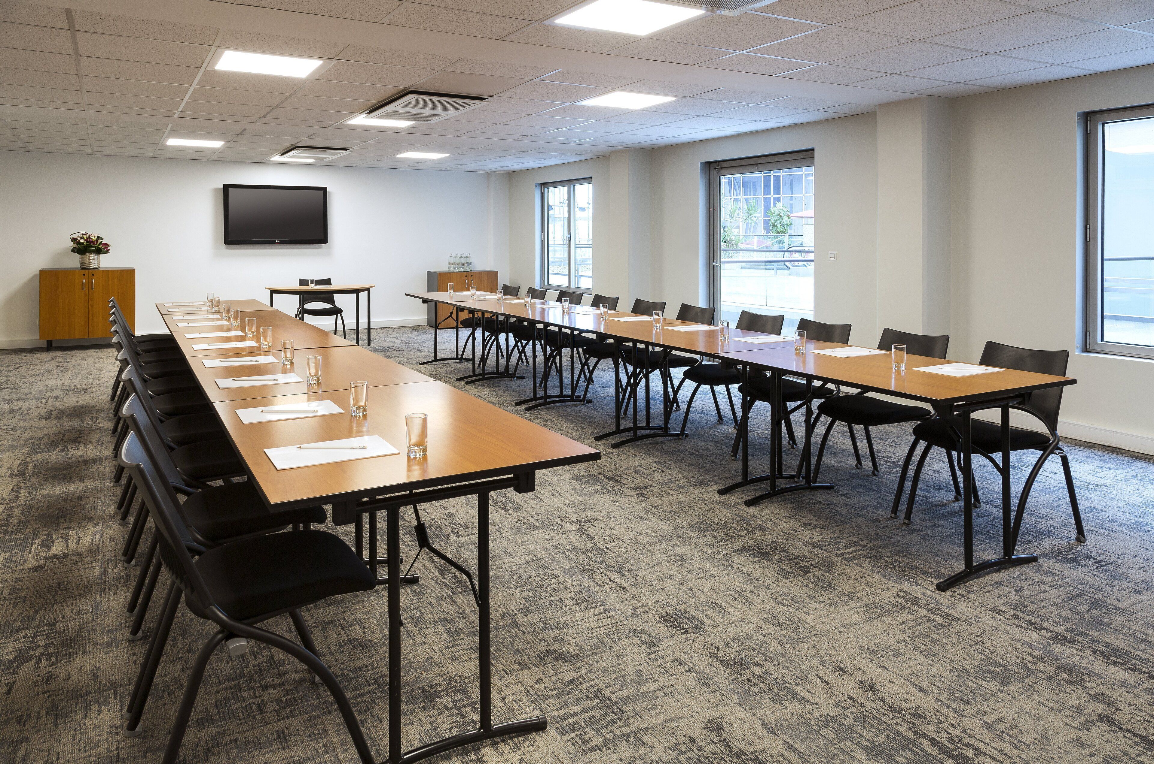 A conference room with a long table, chairs, a television, and windows.