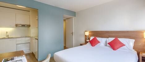 A hotel room with a bed, bedside table, and a kitchenette.