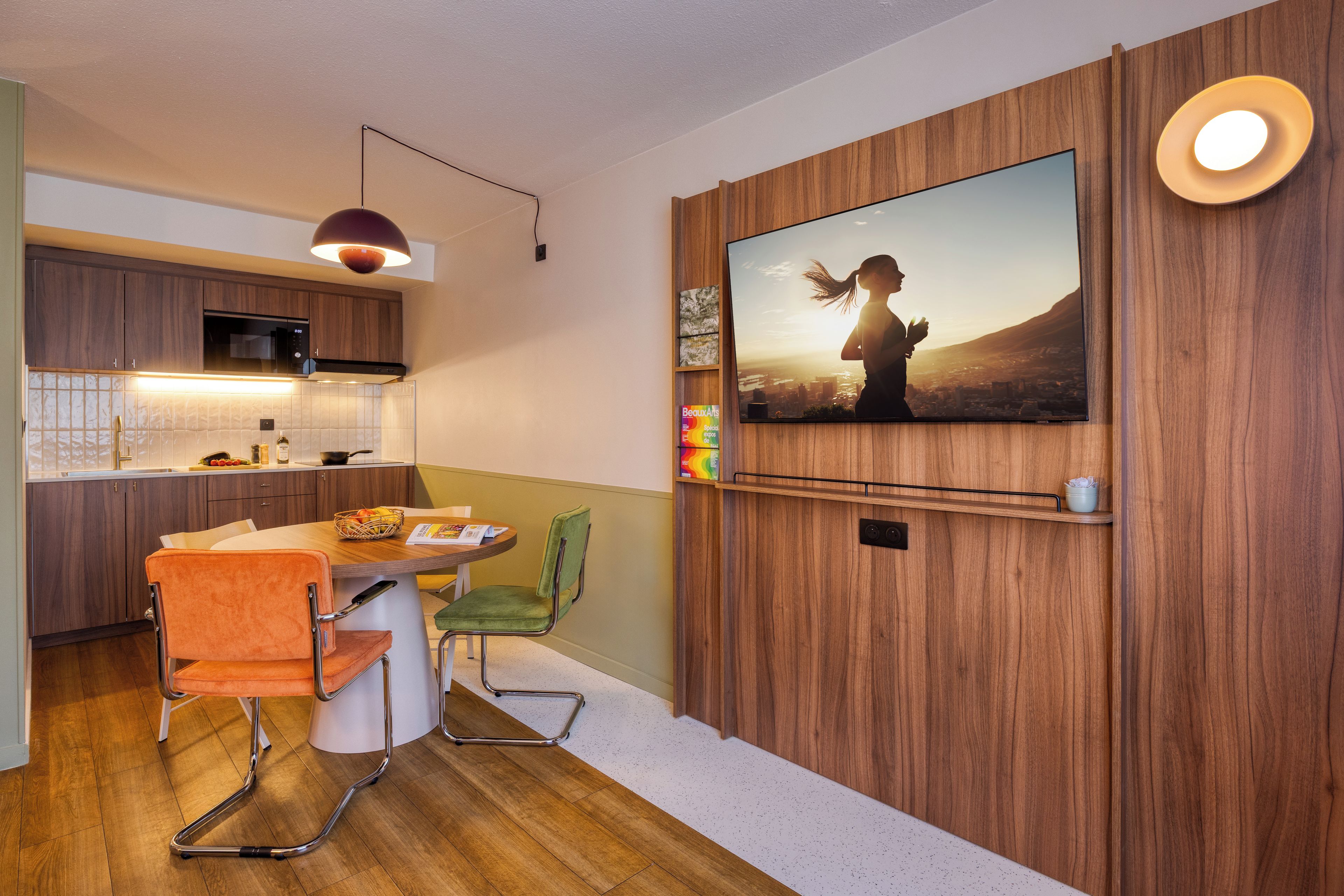 Eine moderne Küche mit Holzausbau, einem Essbereich mit Tisch und Stühlen sowie einem an der Wand montierten Fernseher, der ein Landschaftsbild zeigt.