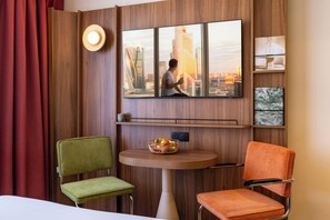 A hotel room with a large window, a flat-screen TV, a small table with a fruit basket, and two upholstered chairs. - Citadines Place d’Italie Paris (Paris)