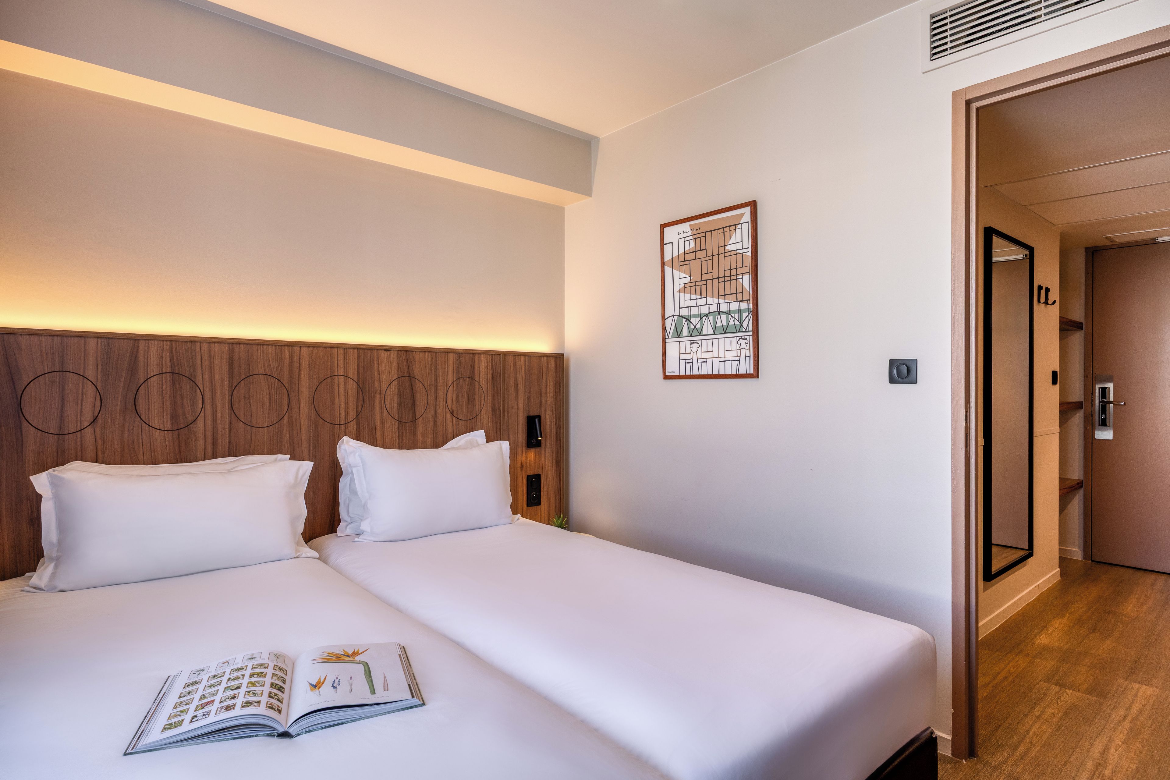 A hotel room with a double bed, a bedside table, a wall-mounted artwork, and a door leading to another room.