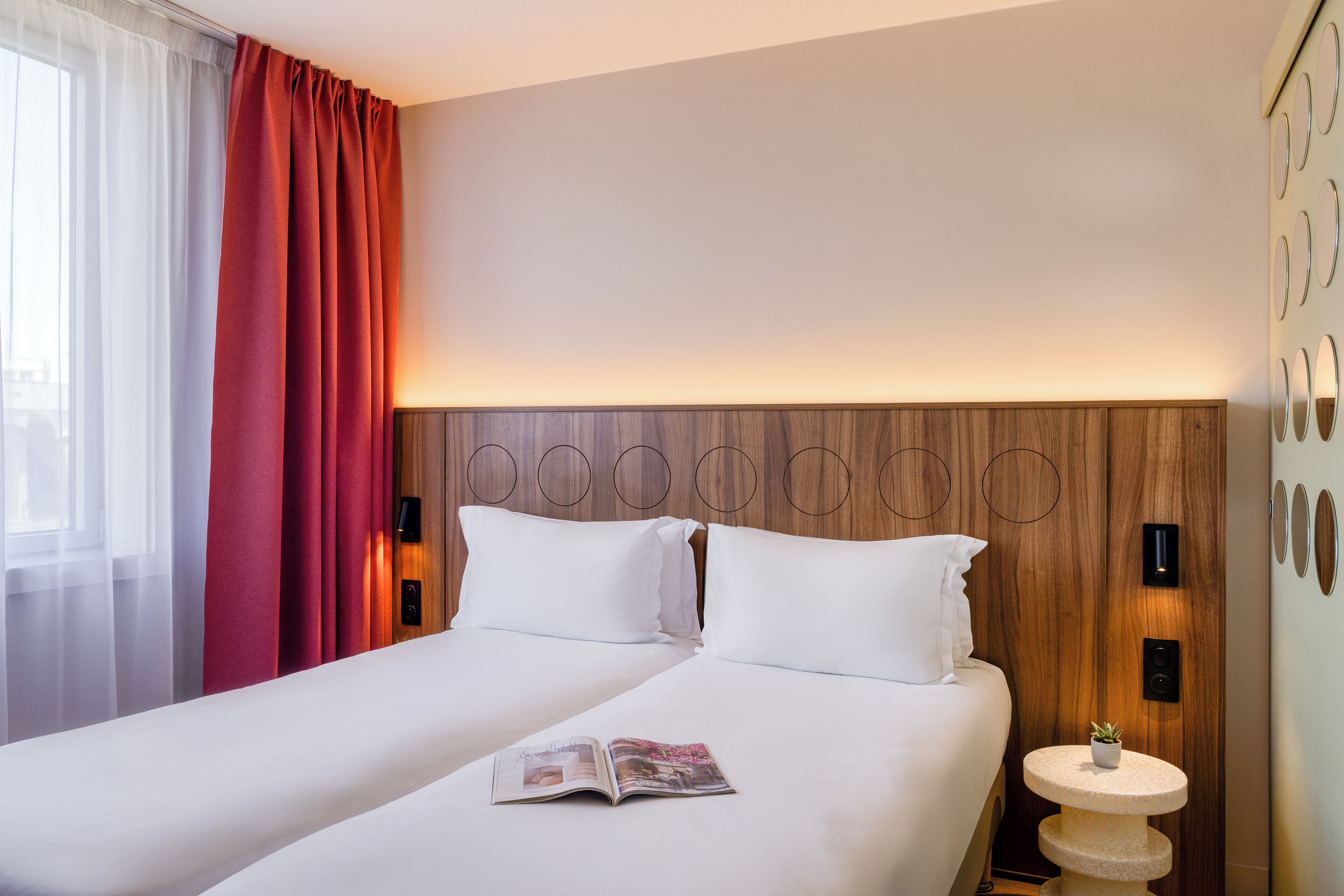 Habitación de hotel con una cama grande, una mesita de noche, una revista y vistas al exterior.
