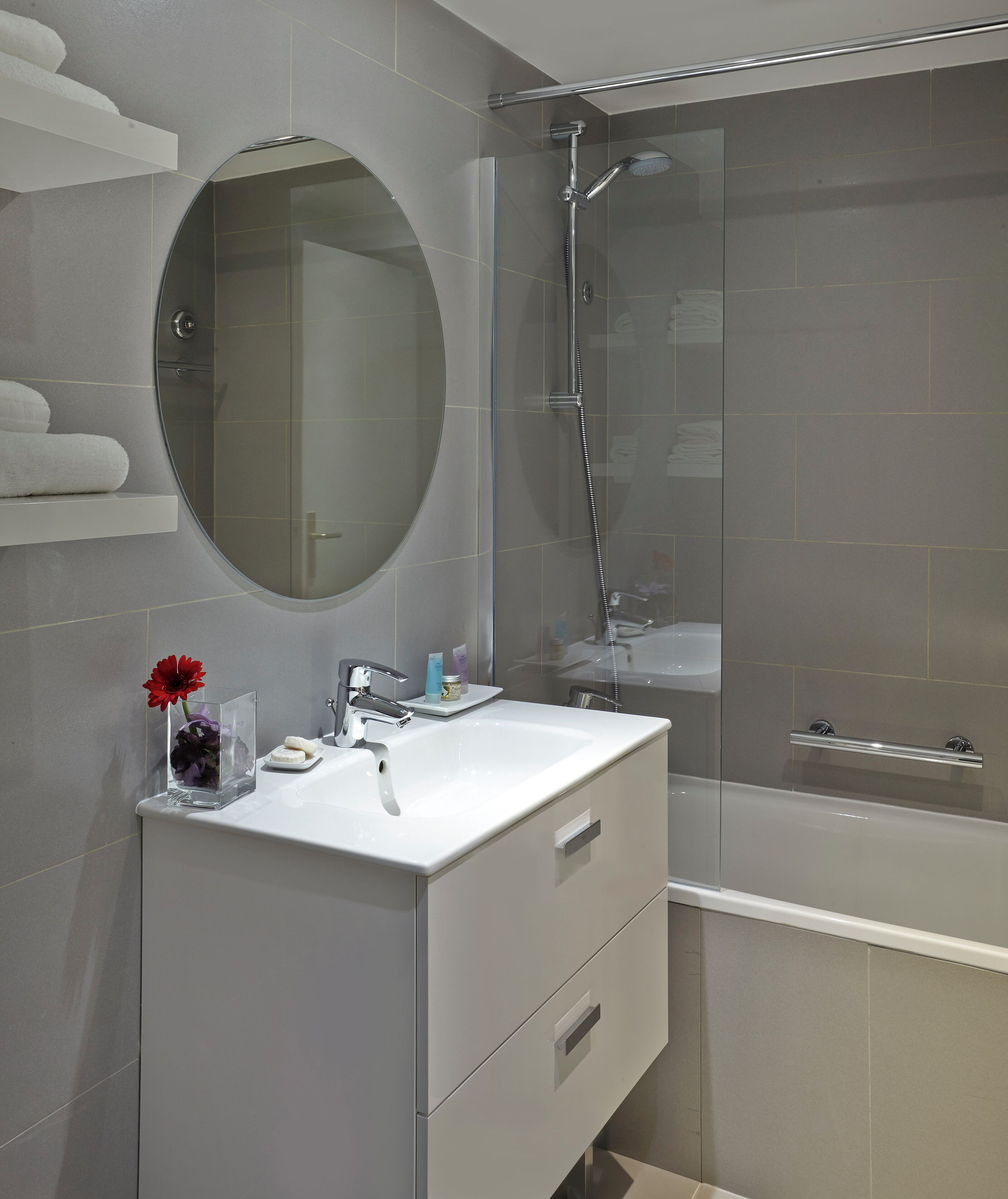 A modern bathroom with a glass-enclosed shower, a round mirror, and a white vanity with a sink.