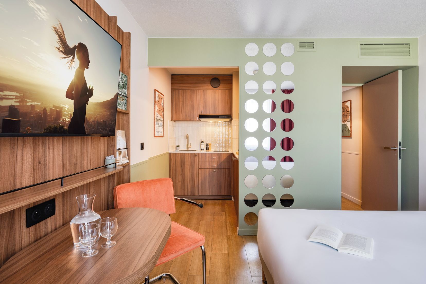 A compact hotel room with a dining area, kitchenette, and a bed.