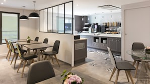 A modern kitchen with a dining area, featuring a large window, pendant lights, and a patterned floor. - Citadines Place d’Italie Paris (Paris)