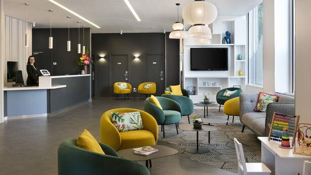 A modern lobby with a reception desk, seating area, and a large TV screen. - Citadines Place d’Italie Paris (Paris)