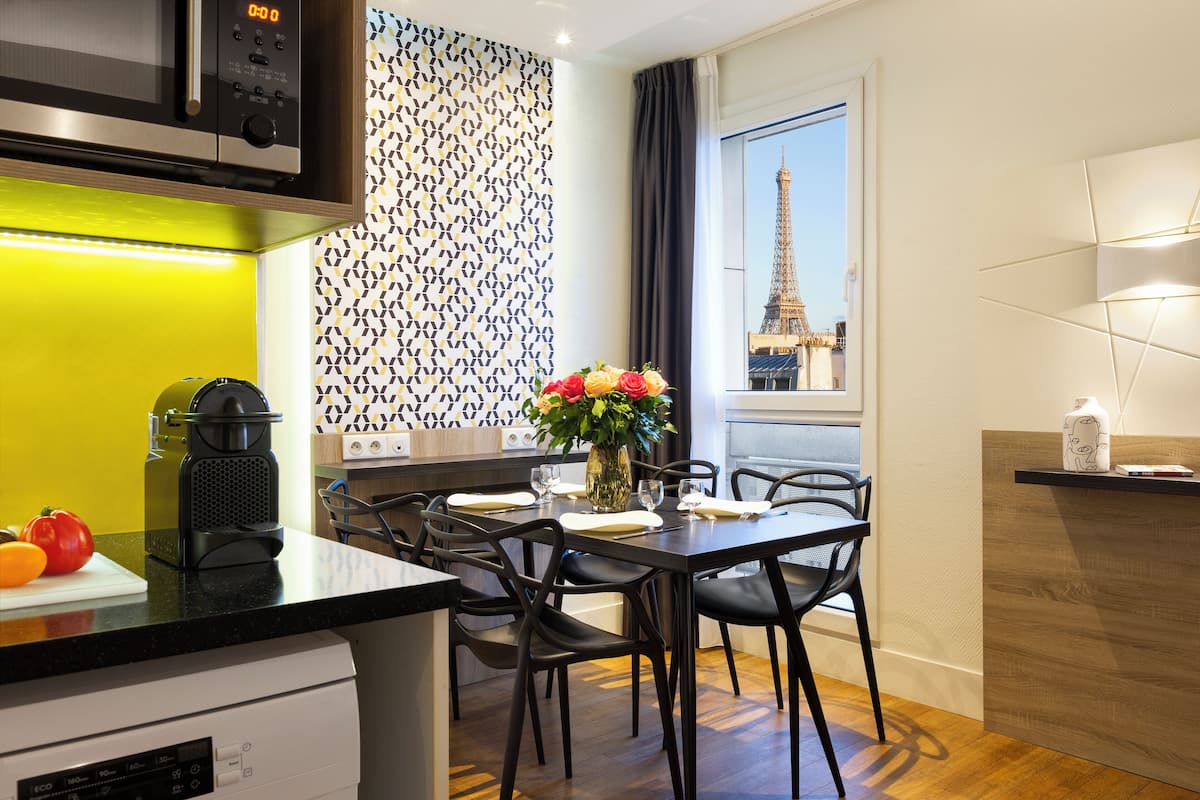 A modern kitchen with a view of the Eiffel Tower, featuring a black countertop, a built-in microwave, and a dining area with a vase of flowers.