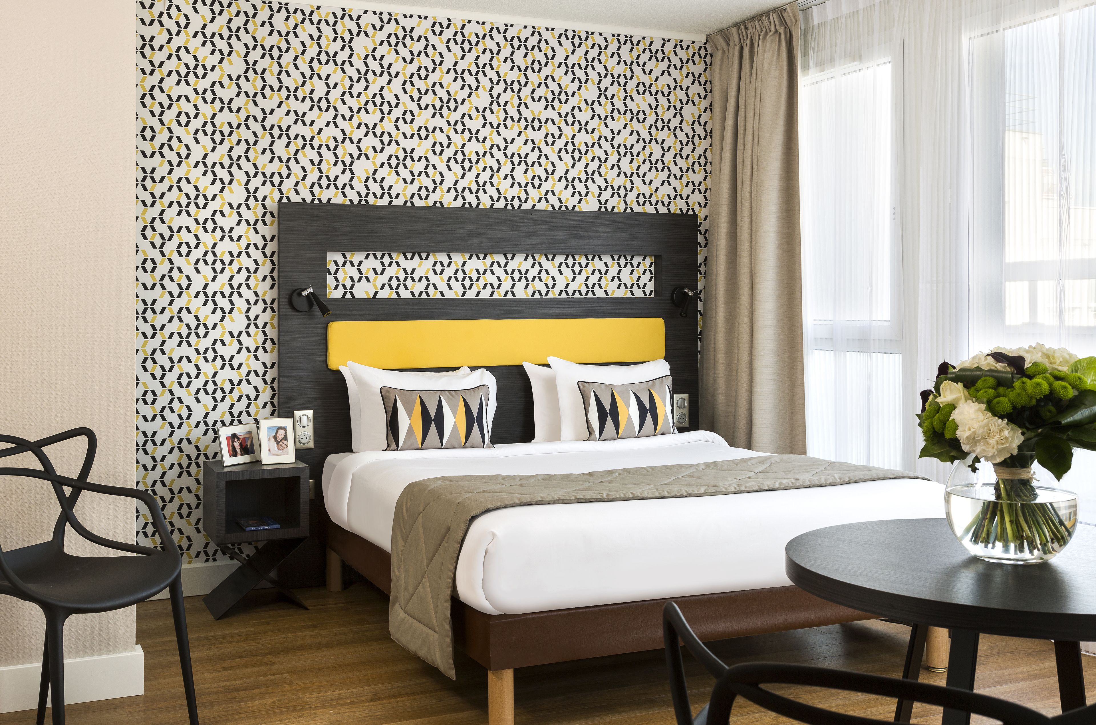 Habitación de hotel ordenada con cama, mesita de noche y una pequeña mesa redonda con un florero.