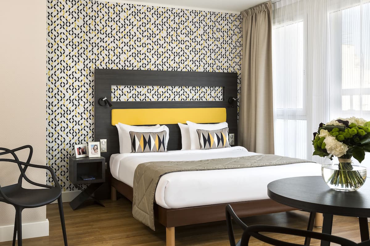 A neatly arranged hotel room with a bed, bedside table, and a small round table with a vase of flowers.