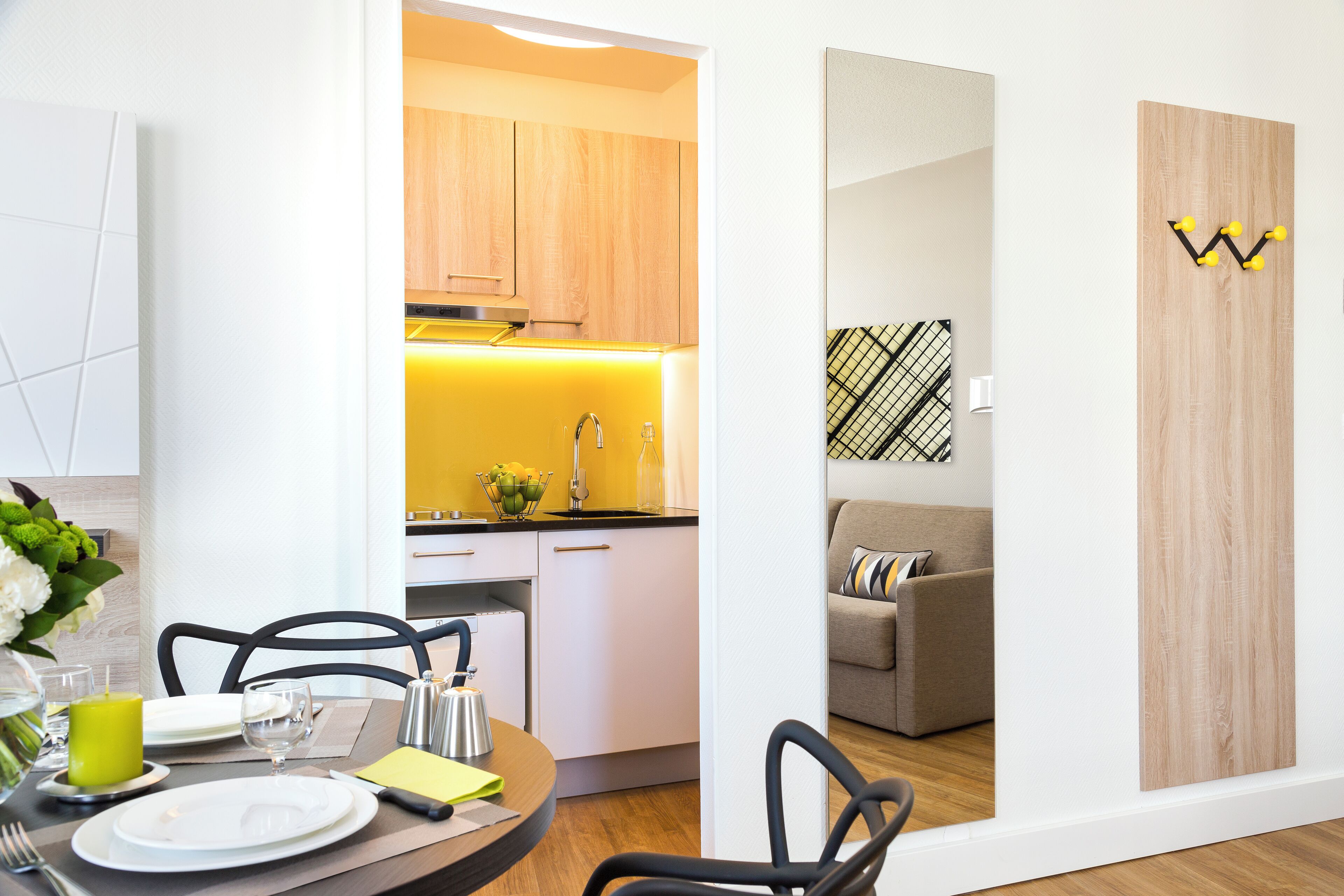 A modern kitchen with wooden cabinets, a yellow-lit countertop, and a dining area with a table set for two.
