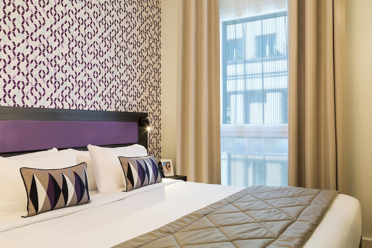 A hotel room with a large bed, a headboard, and a window with curtains.