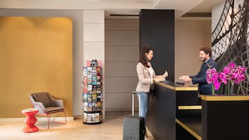 Un espace d’accueil au design moderne, comprenant un comptoir noir, un fauteuil rouge, une petite table et une étagère murale pour exposer des livres.
