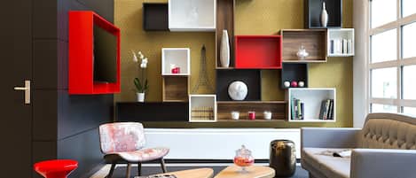 A modern living room with a sofa, two wooden side tables, a red chair, and a television mounted on the wall.