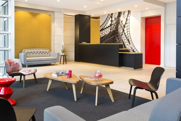 Un moderno vestíbulo con mostrador de recepción, zona de estar y una gran obra de arte de la Torre Eiffel.
