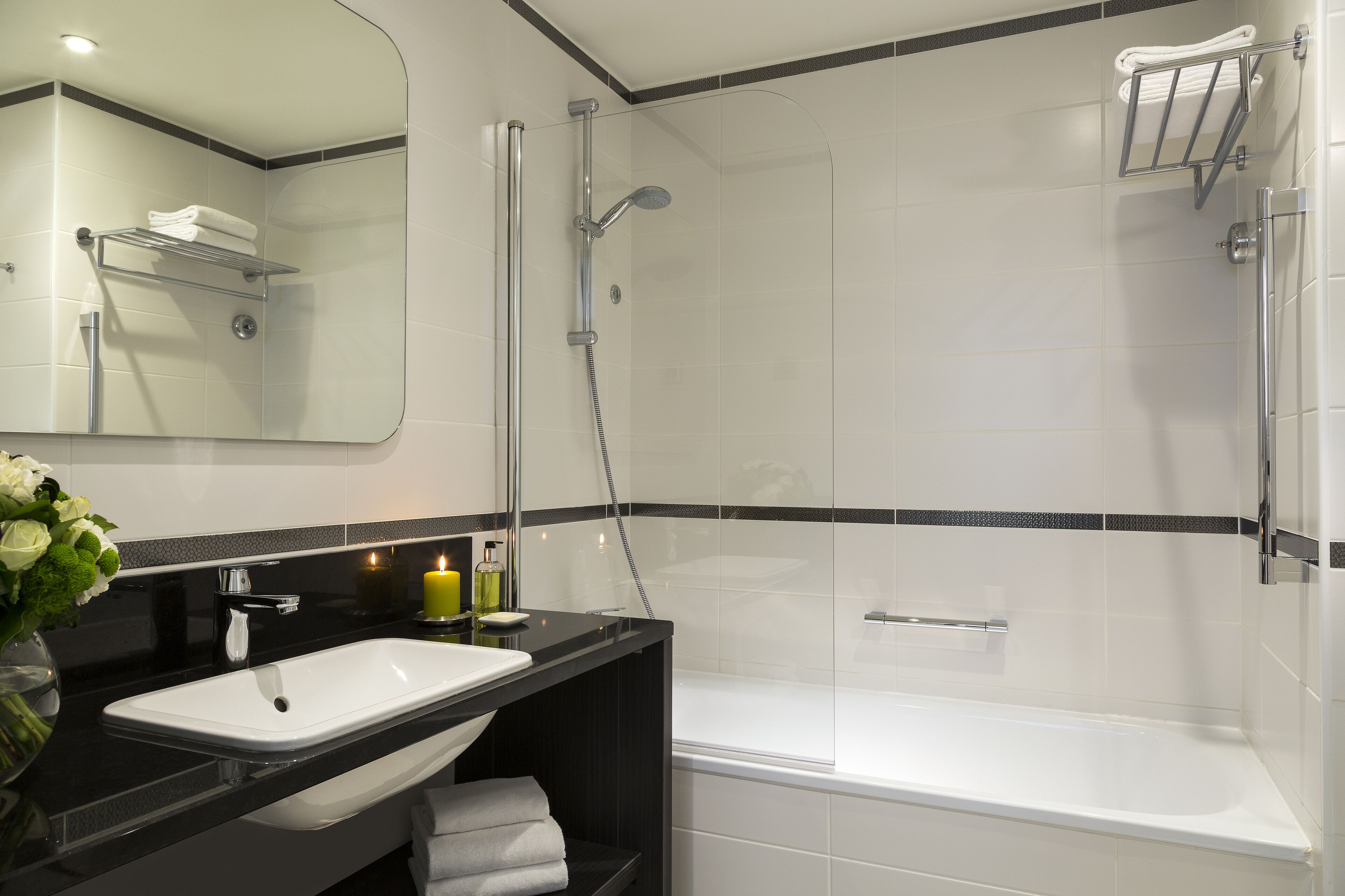 Un baño moderno con un lavamanos blanco, encimera negra y zona de ducha con mampara de vidrio.