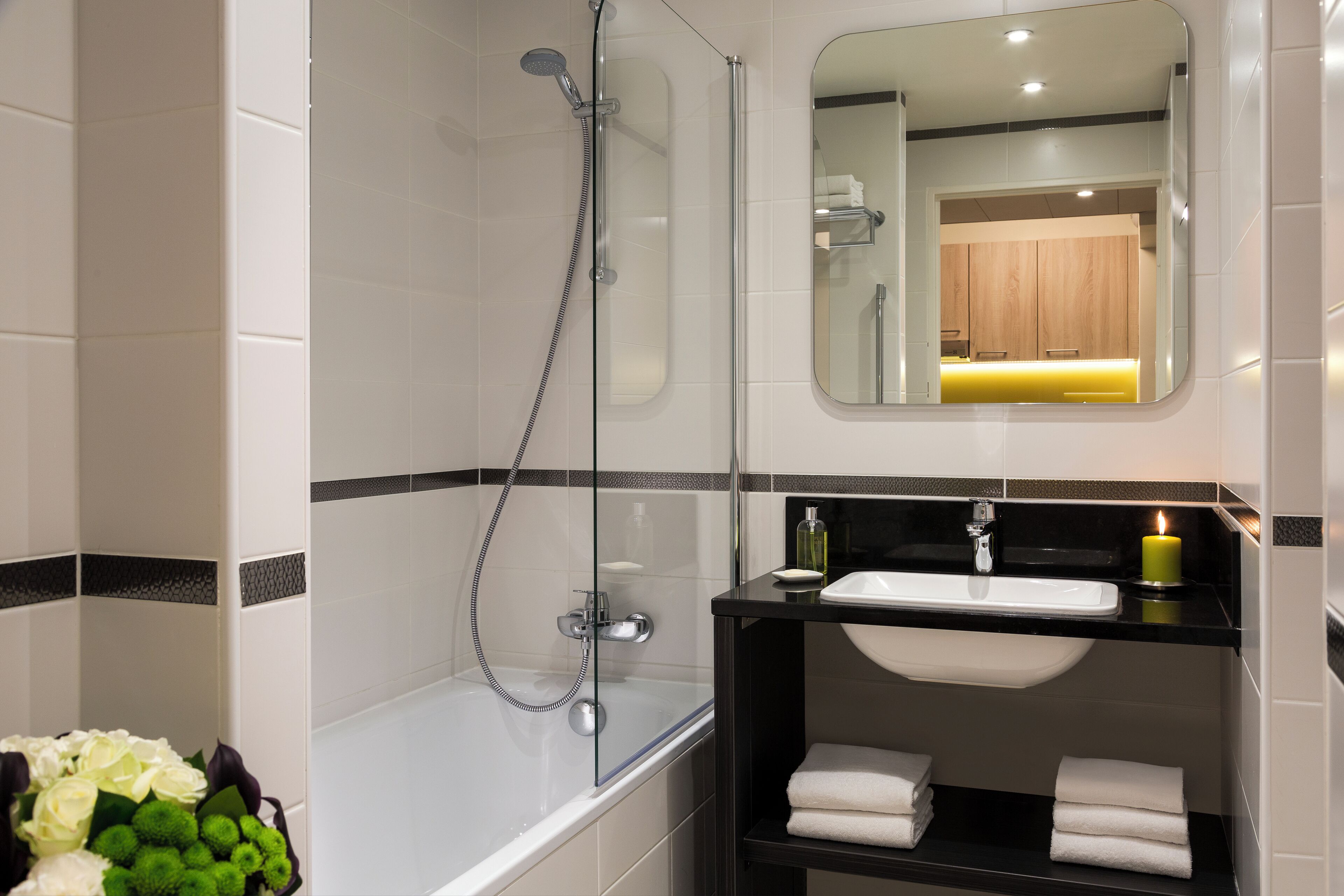 A modern bathroom with a glass-enclosed shower, a white bathtub, a black vanity with a sink, and a mirror above the vanity.