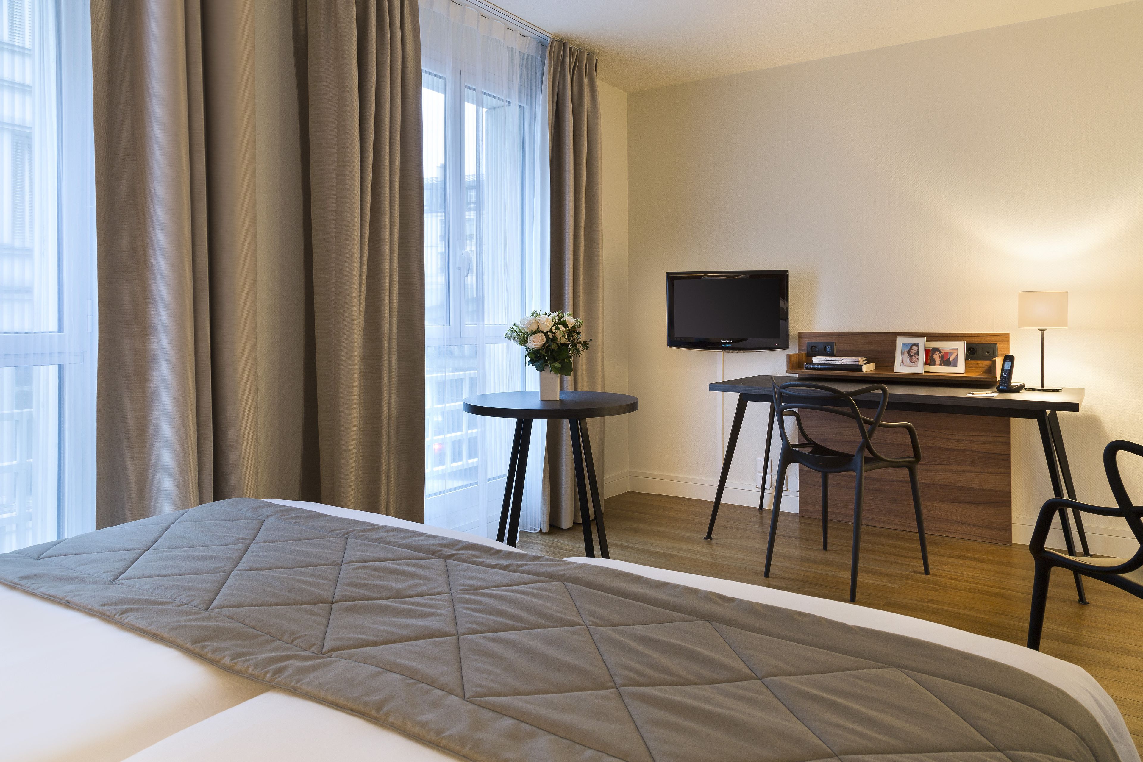 A hotel room with a bed, a desk, a chair, a TV, and a window with curtains.