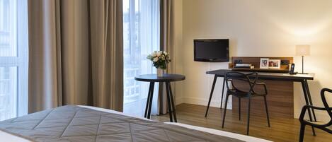 A hotel room with a bed, a desk, a chair, a TV, and a window with curtains.