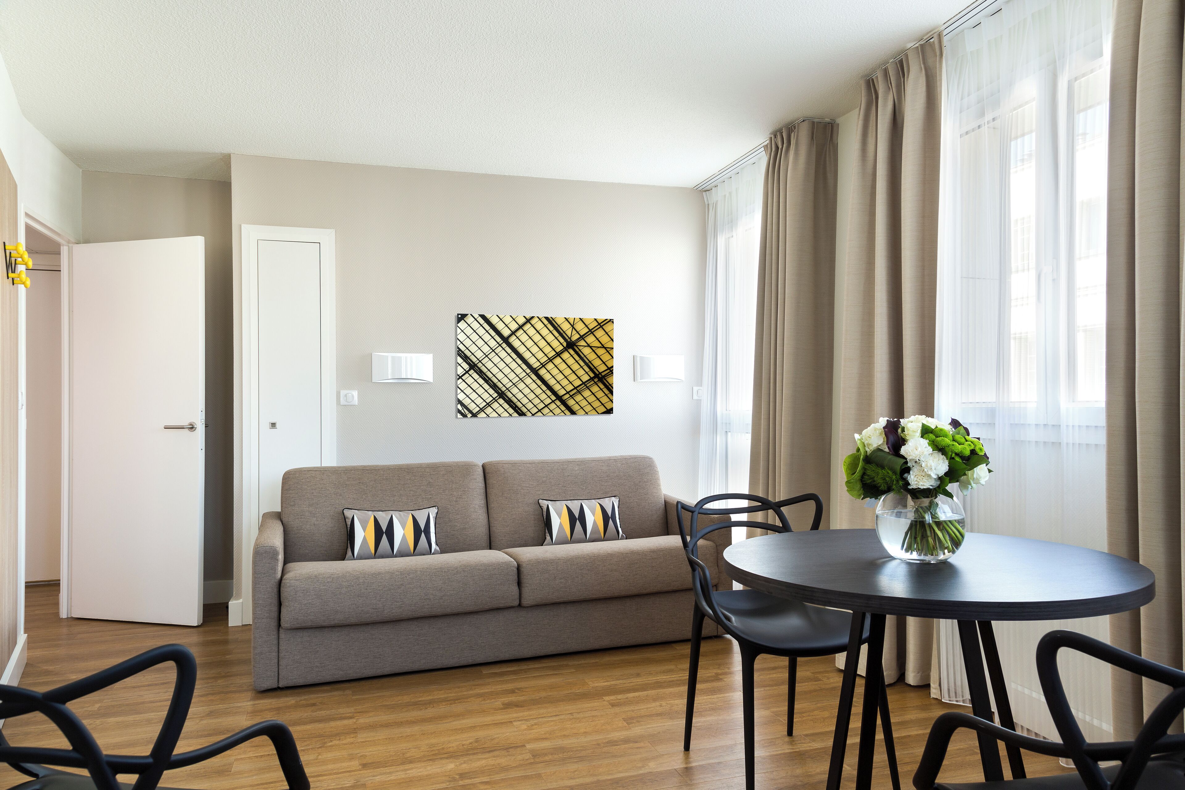A modern living room with a sofa, chairs, a round table, and a vase of flowers.