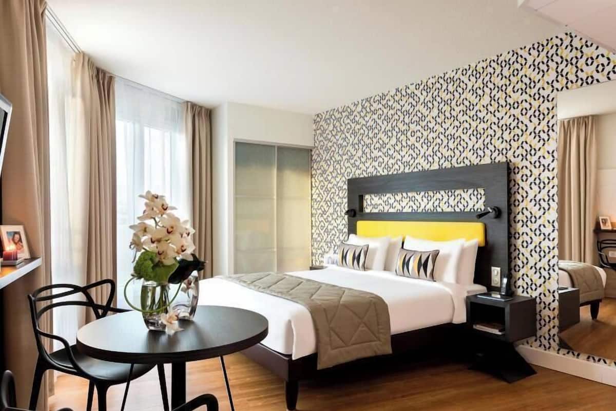 A hotel room with a bed, bedside table, lamp, chair, and a round table with a vase of flowers.