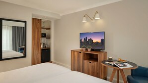 A hotel room with a large bed, a TV on a wooden stand, a small table with a cup and pastries, and a mirror with curtains. - Citadines Barbican London (London)