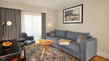 Una sala de estar moderna con un sofá azul, una mesa de comedor con sillas, un frutero y una mesa de centro con una bebida y un plato.