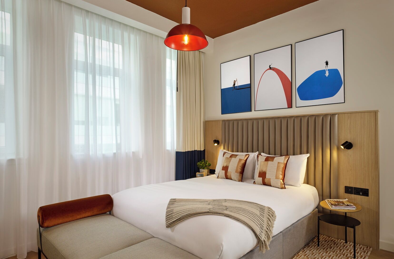 Una camera d'albergo moderna con un letto grande, una lampada a sospensione rossa e tre opere d'arte incorniciate sopra il letto.
