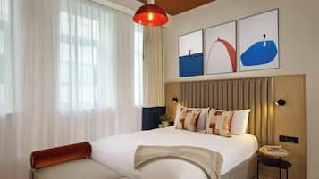 Una camera d'albergo moderna con un letto grande, una lampada a sospensione rossa e tre opere d'arte incorniciate sopra il letto.