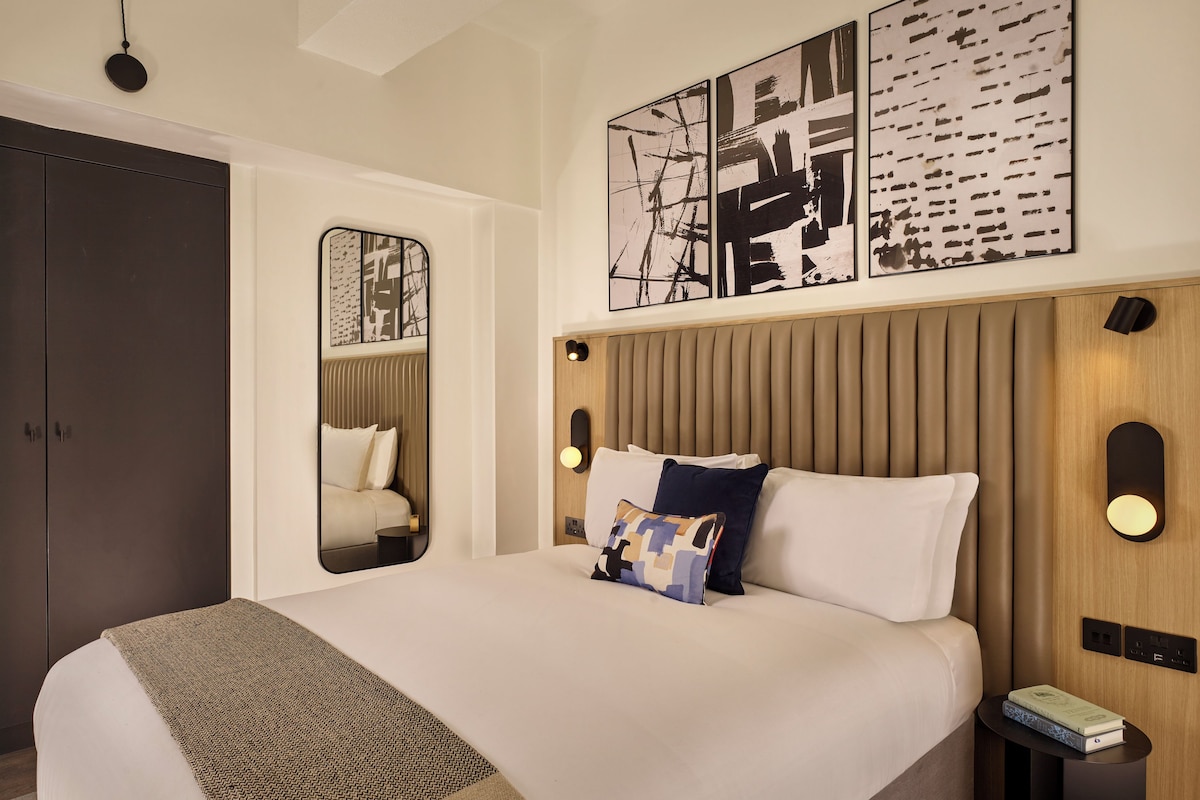 A modern hotel room with a large bed, a mirror, and artwork on the wall.