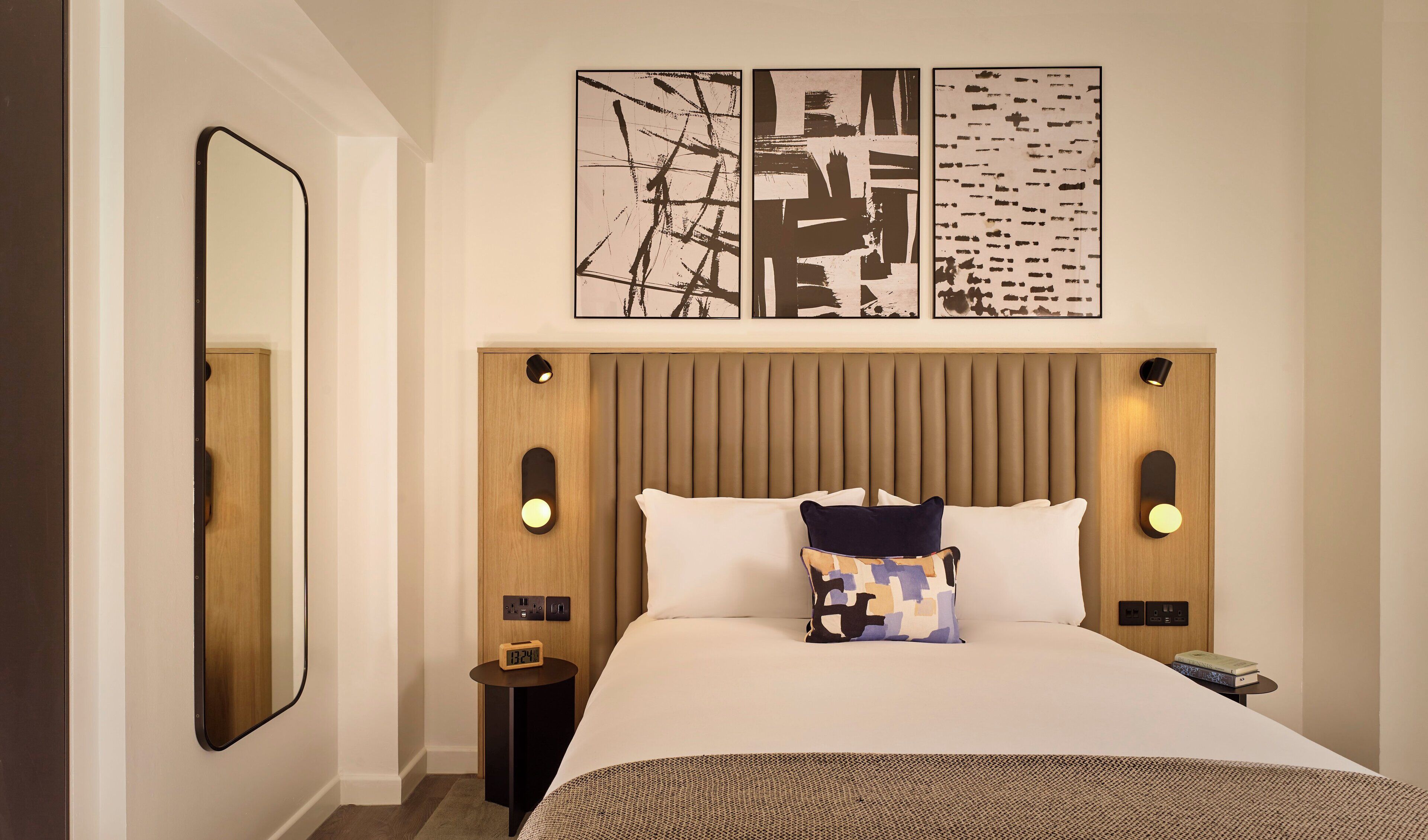 A hotel room with a large bed, a wooden headboard, wall-mounted artwork, and bedside lamps.