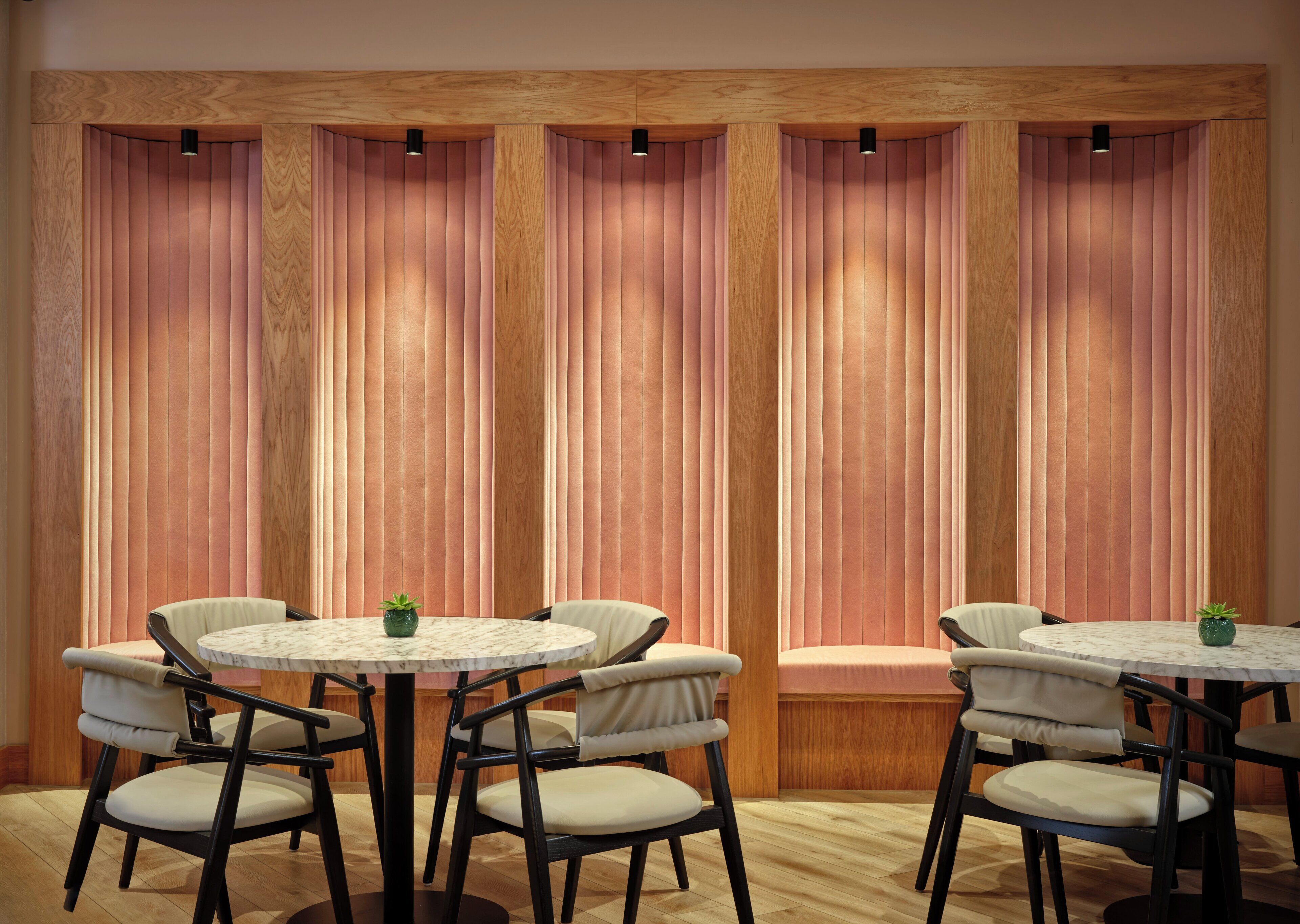 A room with four round tables and chairs, a bench, and a wooden panel wall with vertical slats.