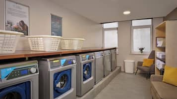 A laundry room with multiple washing machines, baskets, and a seating area with a window.