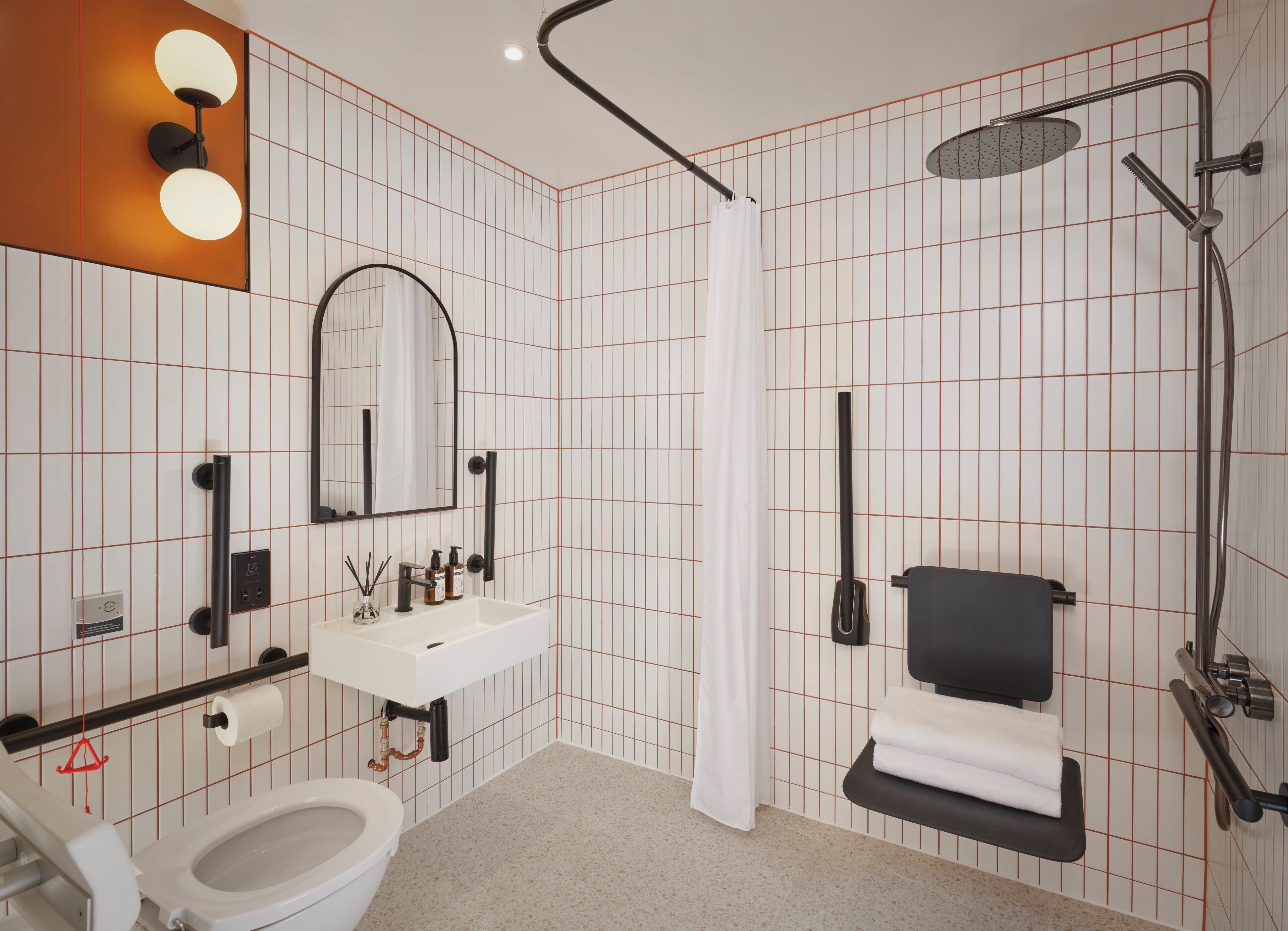 A modern bathroom with a toilet, sink, mirror, shower, and towel rack.
