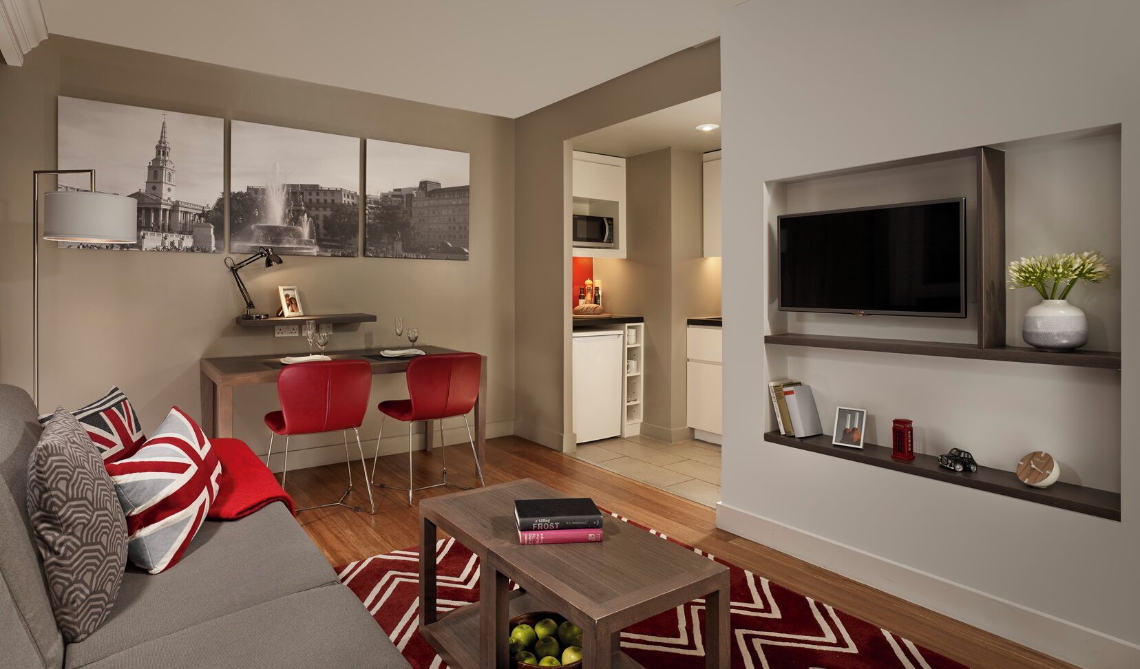 Een moderne woonkamer met een bank, rode stoelen, een salontafel en een aan de muur bevestigde televisie.
